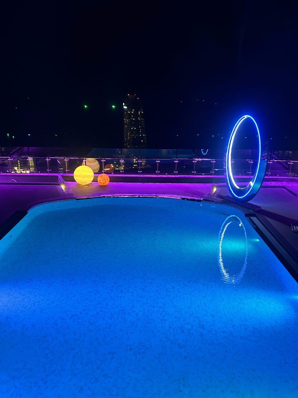 Swimming pool at night with glowing planet lamps and a blue ring sculpture